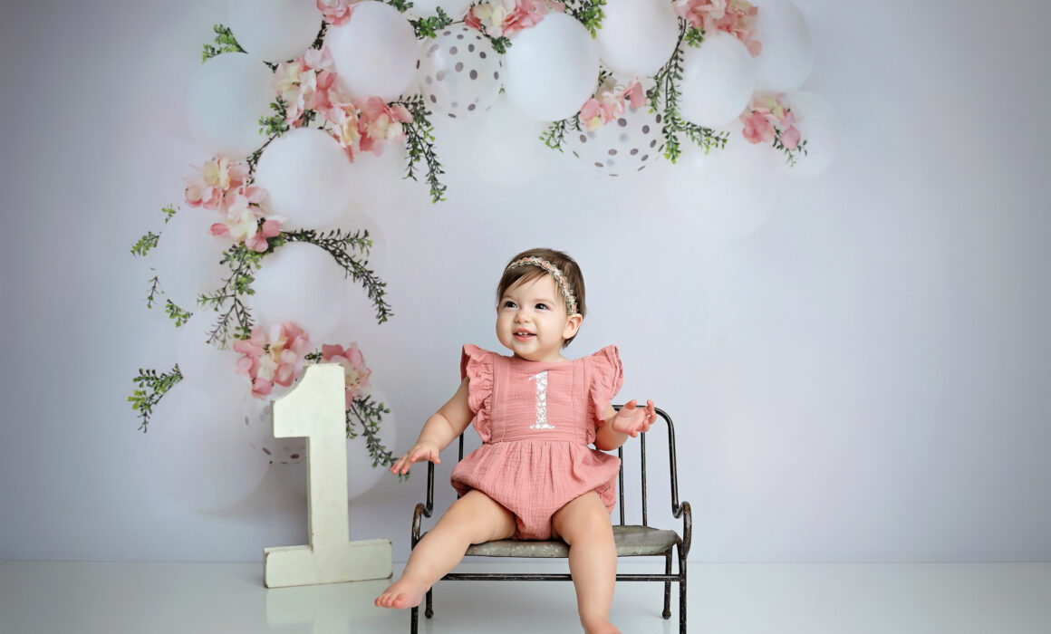 Smiling one-year-old girl in a dusty rose romper during her San Antonio first birthday session