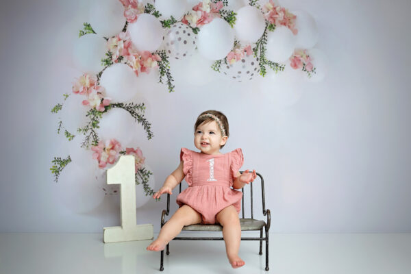 Smiling one-year-old girl in a dusty rose romper during her San Antonio first birthday session