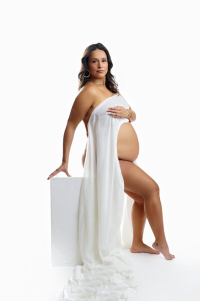 Pregnant mother seated on a white cube wearing elegant draped white fabric