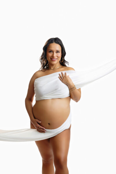 Expecting mother posing with flowing white fabric against a white studio background