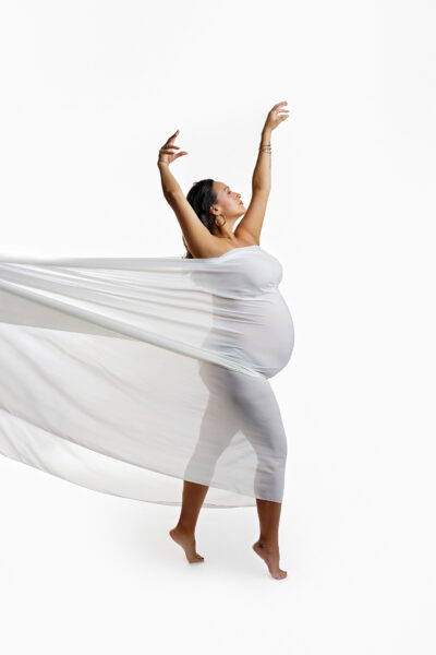 Pregnant mother posing with raised arms and flowing white fabric