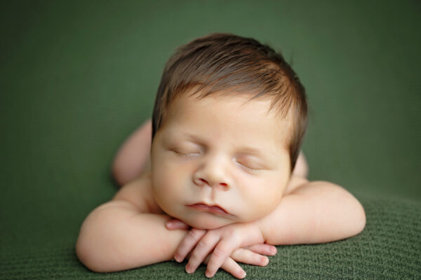 Close-up portrait of a sleeping newborn baby boy with hands tucked under his chin.