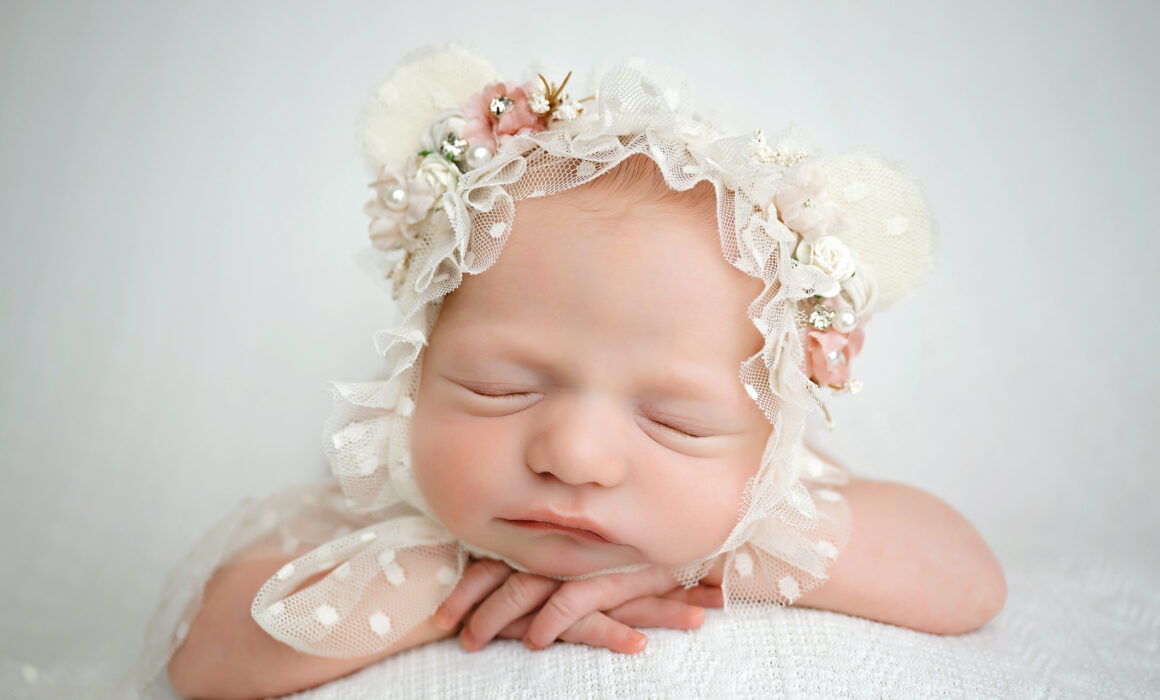 Sleeping newborn baby girl wearing a cream floral teddy bear bonnet during her San Antonio newborn photography session. Copy 2. Curled-Up Baby Pose