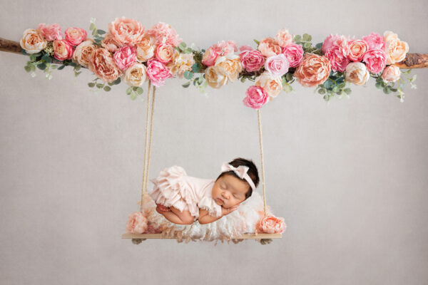 Newborn baby girl posed on floral swing in pink newborn photography composite