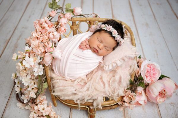 Newborn baby girl wrapped in blush pink with delicate floral headband and peach blossoms