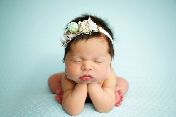Sleeping newborn baby girl posed with chin resting on hands against soft mint background