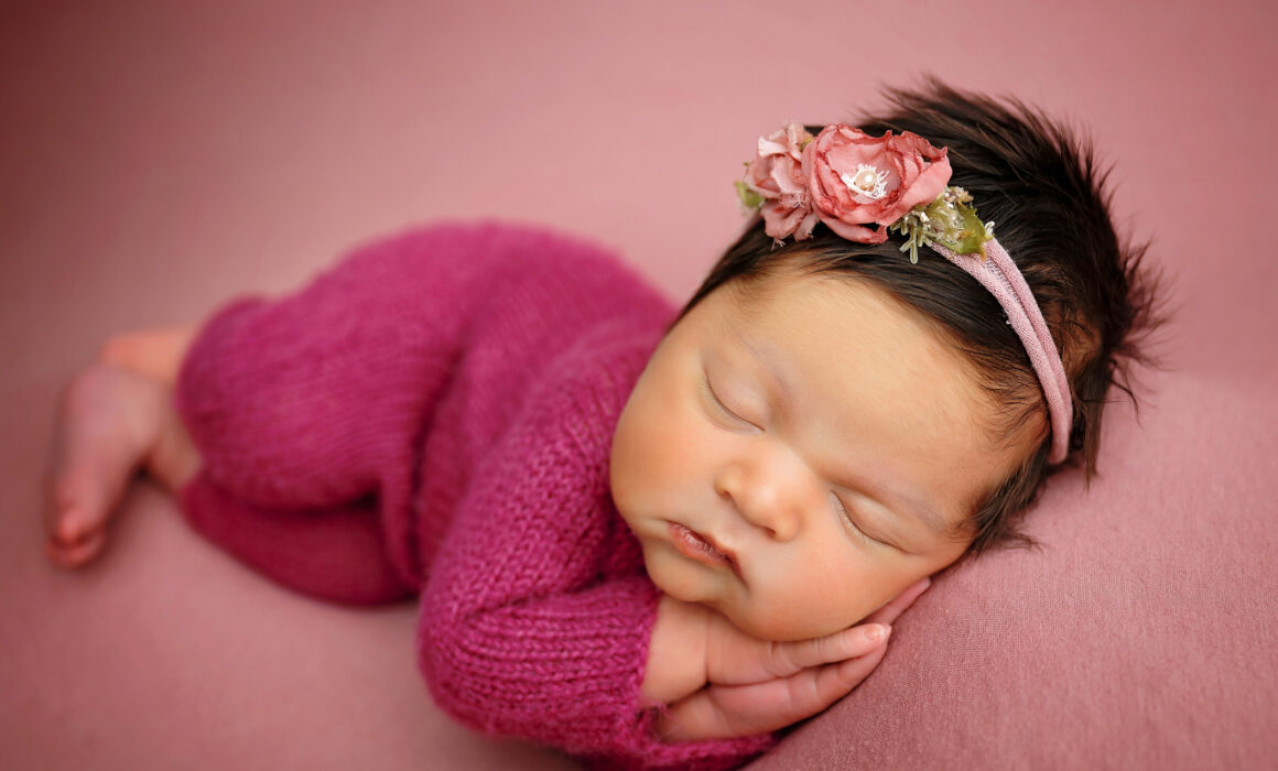 Newborn baby girl wearing magenta knit outfit and floral headband