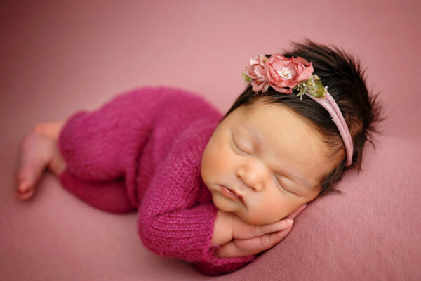 Newborn baby girl wearing magenta knit outfit and floral headband