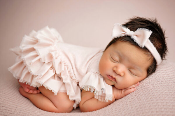 Sleeping newborn girl in pale pink ruffled outfit with matching bow