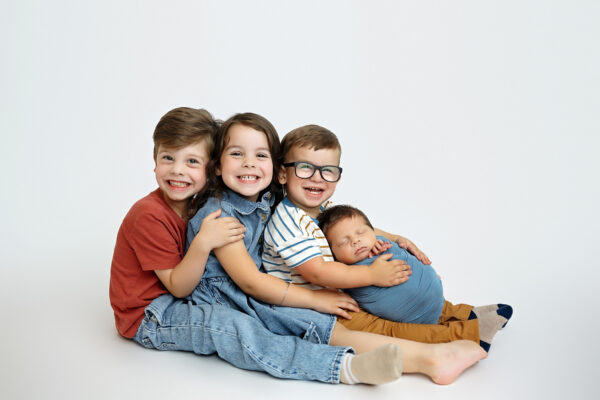 Three older siblings posing with their newborn baby brother during a San Antonio newborn session.
