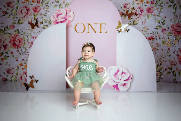 Baby girl celebrating her first birthday in a sage green dress with pink flowers and butterflies