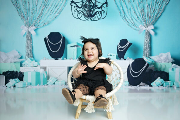 Happy baby girl laughing in a black birthday outfit surrounded by Tiffany blue gift boxes and pearl decorations.