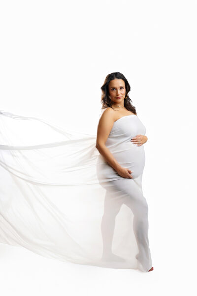 Side portrait of expecting mother with sheer white fabric flowing behind her