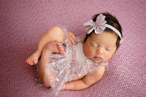 Newborn girl in sparkly blush pink outfit and matching bow
