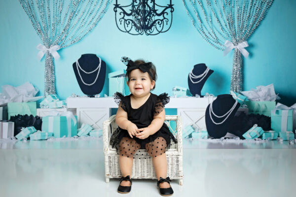Sweet baby girl smiling in a black tulle birthday dress and matching bow with turquoise and pearl birthday decorations.