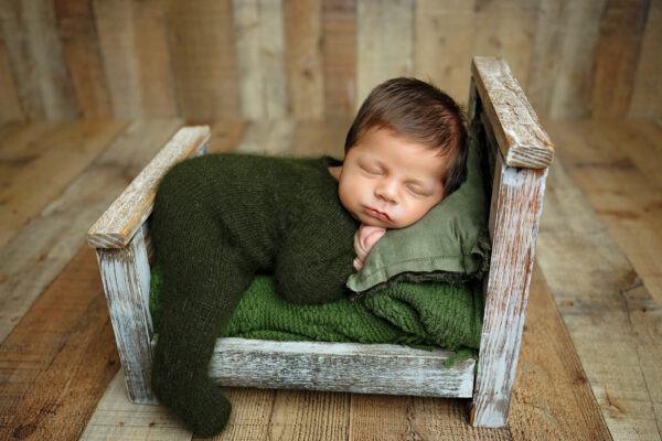Newborn baby boy sleeping in a rustic wooden bed during a San Antonio studio session.